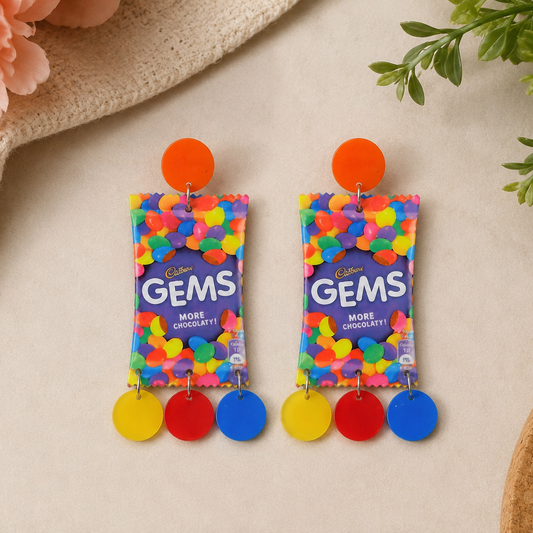 Earrings designed like Cadbury Gems packaging on a neutral background with floral and plant elements.