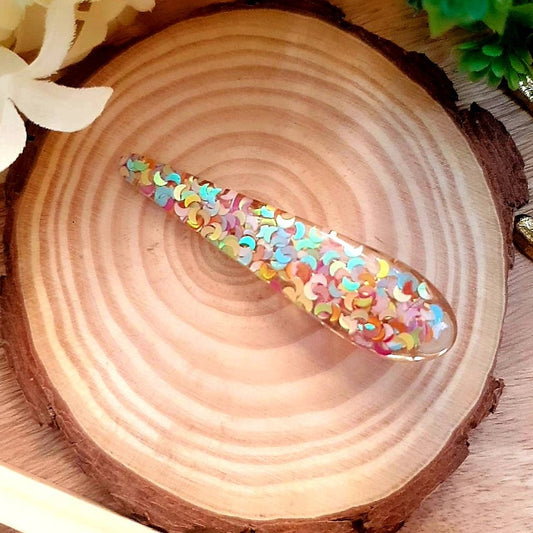 Our Rainbow Resin Clip is a unique accessory to make you stand out from the crowd. This handmade clip is crafted of decorative resin and is decorated with beautiful rainbow-coloured, shiny sequins. It reflects the light and gives a stylish finish to any look.