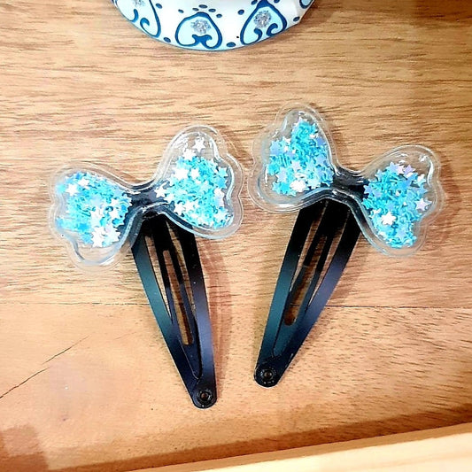 This set of two vibrant blue Tic-Tac Clip shaker bows provides a stylish and unique way to accessorize. Each clip is filled with glimmering blue sequins, sure to make any outfit special. Get creative and make a statement with these eye-catching accessories!