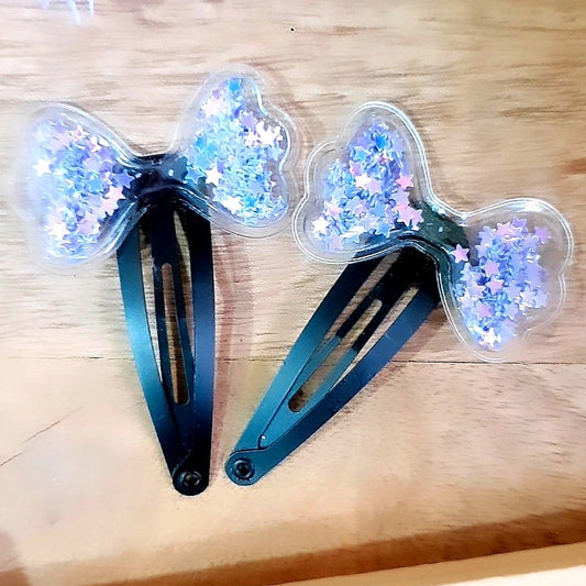 These Purple Tic-Tac Clips provide a fashionable way to decorate your hair. Filled with shiny star sequins, these clips come in a set of two and are perfect for adding a touch of sparkle to any hairstyle. Featuring a cute shaker bow design, these clips are sure to become your go-to accessories.