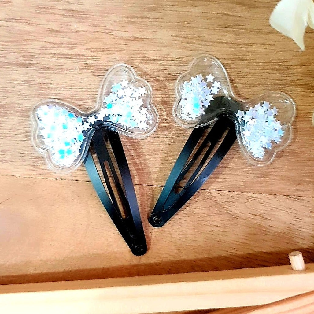 Our White Tic-Tac Clips come in pairs, perfect for adding a unique look to your hair. These clips feature bow-shaped shakers with shiny white star sequins for a sparkly, eye-catching effect. Get a fun and stylish look with these cute clips.