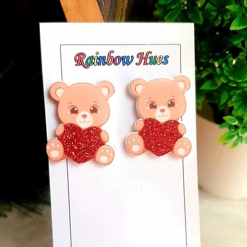 Show your love with Teddy Heart Studs! These beautiful earrings combine a classic teddy bear motif with pure romance. Guaranteed to add a touch of sweetness to any look!  Adorable teddy bears holding glitter red hearts